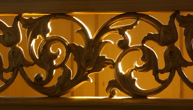 A wrought iron rail, backlit in a warm glow, flourishes with detail 