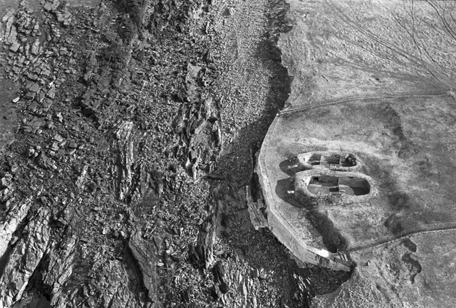 Black and white aerial photograph of the Knap of Howar, Papa Westray. The images shows the dwellings on the right with the coastline cutting the image in two.  